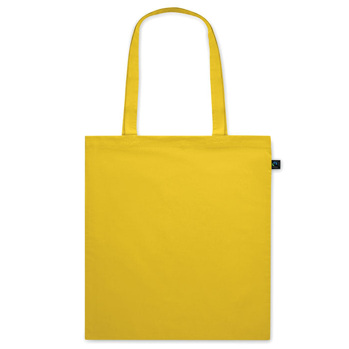 Bolsa de tela amarilla OSOLE COLOUR con asas largas y etiqueta de comercio justo. Perfecta para ferias, regalos y campañas promocionales.