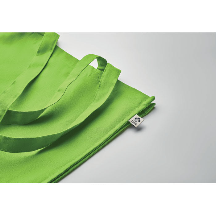 Detalle de la bolsa verde lima BENTE COLOUR con etiqueta ecológica, ideal como bolsa de tela promocional y reutilizable.