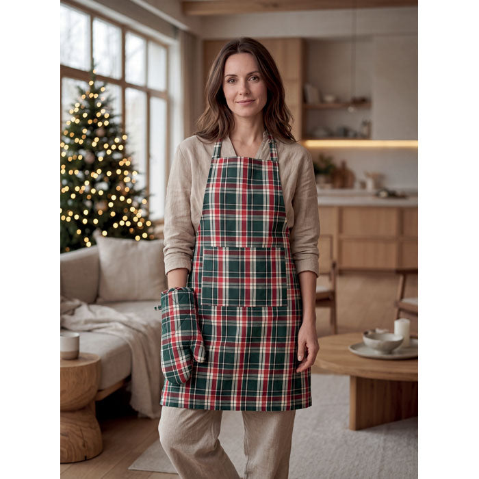 Mujer usando SANTAPRON - Set cocina algodón a cuadros en la cocina con luces de árbol de Navidad de fondo.