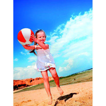 Niña jugando en la playa con pelota hinchable blanca y roja