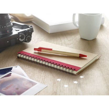 Cuaderno de cartón con espiral y bolígrafo en una mesa al lado de una taza, unas fotos y una cámara