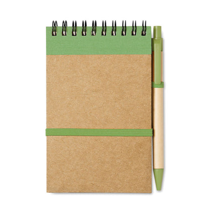 Libreta a6 con espiral en parte superior y detalles en color naranja, goma horizontal de cierre y soporte para boli color naranja y bolígrafo de cartón con detalles en verde