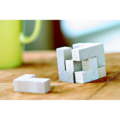 Puzzle 3D en forma de cubo de madera con pieza suelta sobre mesa de madera