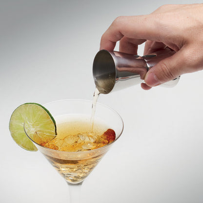 Mano sirviendo licor en una copa desde vaso medidor de bebidas