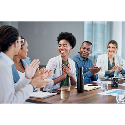 Gente sonriendo en mesa de trabajo con botella negra
