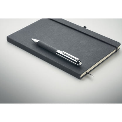 Bolígrafo negro metálico sobre cuaderno negro con cierre goma y fondo gris