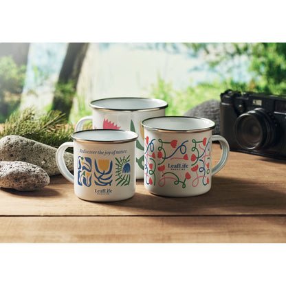 3 tazas metálicas de diferentes tamaños personalizadas con coloridos diseños sobre una mesa de madera