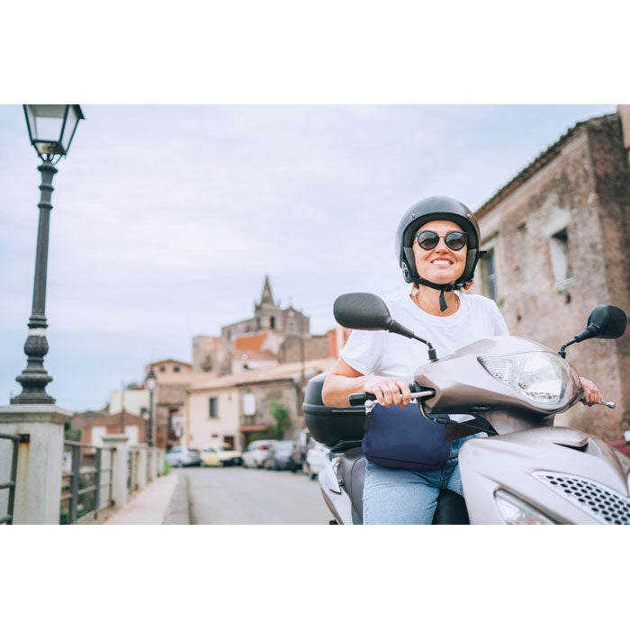 Mujer sonriente sobre una moto, usando casco y gafas de sol, con riñonera RPET 300D visible, en un entorno urbano.