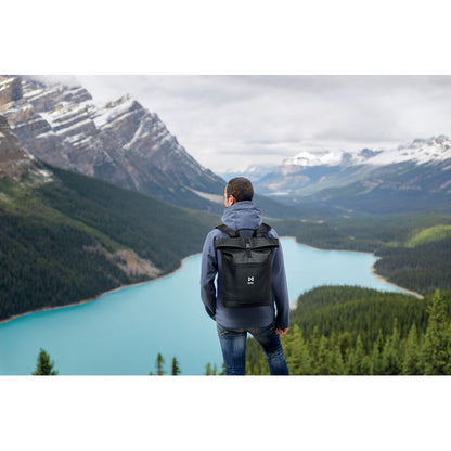 Mochila con cierre rolltop personalizada con logotipo y a la espalda de un hombre en un paisaje de montaña