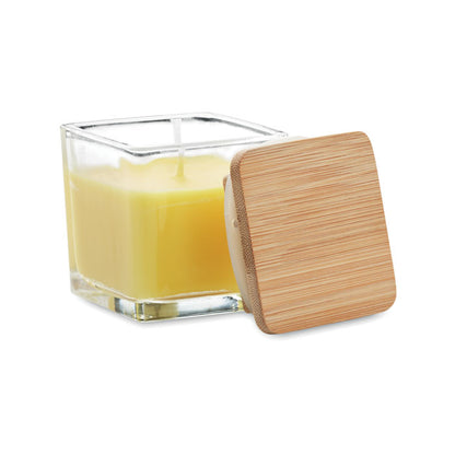 Vela cuadrada amarilla con envase de vidrio y tapa de madera a un lado