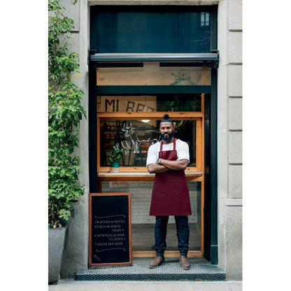 Camarero con delantal burdeos en la puerta de una cafetería