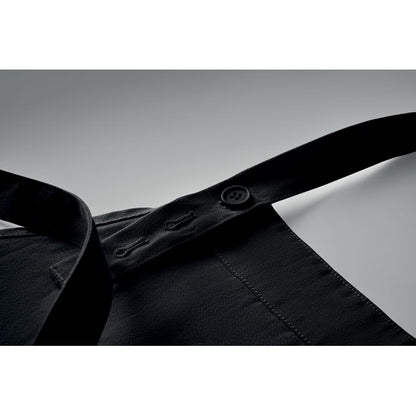 Detalle de cinta ajustable con botones de un delantal negro