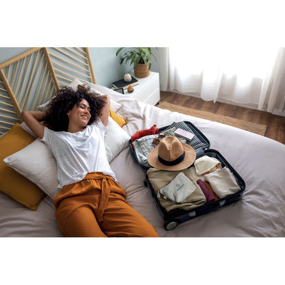 Mujer tumbada en cama con maleta con neceser blanco