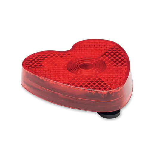 Vista lateral de un reflector rojo en forma de corazón, fabricado en ABS, con clip trasero para fácil sujeción.