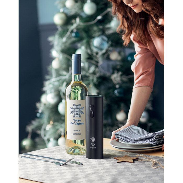 Vista de una botella de vino blanco junto a un abridor eléctrico de botellas VINO en un ambiente festivo.