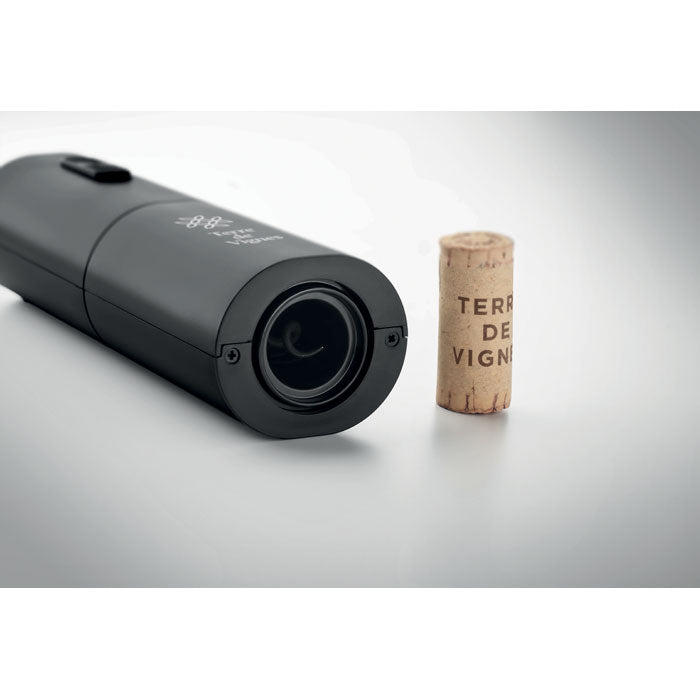 Acercamiento a un abridor eléctrico de botellas de color negro mate junto a un corcho de vino.