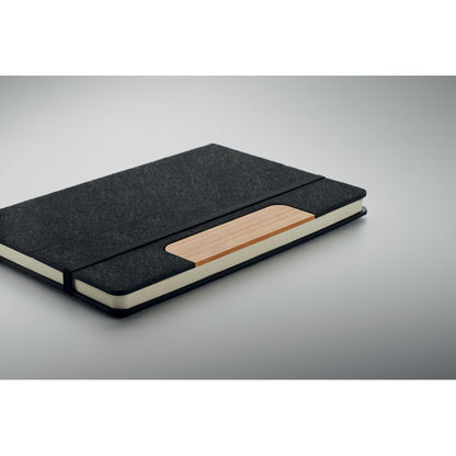 Libreta negra con cierre de goma negra y pieza de bambú en la portada sobre una superficie gris