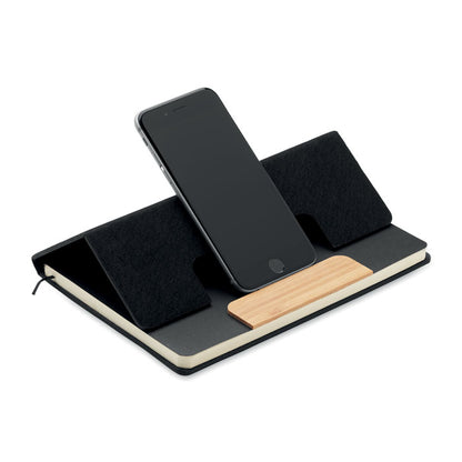 Libreta negra con portada plegable donde se coloca un teléfono móvil que se apoya sobre la pieza de bambú de la portada y así se mantiene de pie y la libreta actua de soporte de teléfono