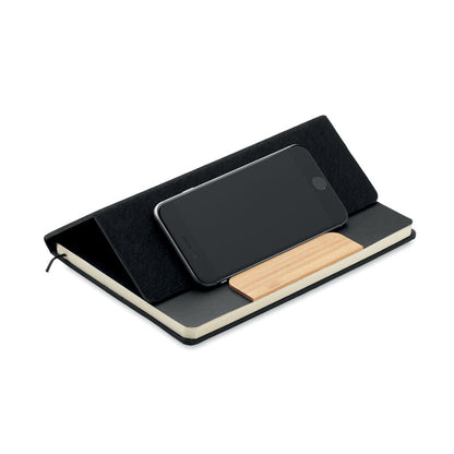 Teléfono movil colocado en horizontal sobre libreta negra con portada plegada y apoyado en la pieza de bambú de la portada de la libreta
