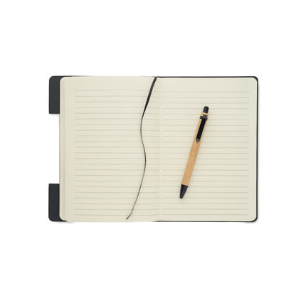 Cuaderno abierto con hojas rayas color crema, cinta marcapáginas de tela negra y bolígrafo de madera con detalles de plástico 