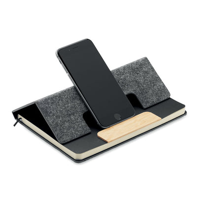 Libreta gris con portada plegable donde se coloca un teléfono móvil que se apoya sobre la pieza de bambú de la portada y así se mantiene de pie y la libreta actua de soporte de teléfono