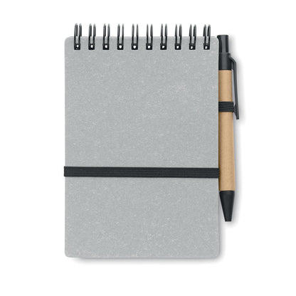 Cuaderno de tapas de cartón grises,  cierre con goma elástica, encuadernación en la parte superior con espiral negra y con bolígrafo de cartón con clip, punta y pulsador negro unido a la libreta con una goma negra