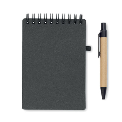 Portada de libreta negra de cartón con espiral negra en la parte superior y bolígrafo de cartón con detalles en plástico negro