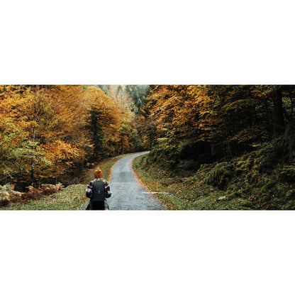 Foto de árboles en otoño y chica de espaldas con mochila negra de RPET