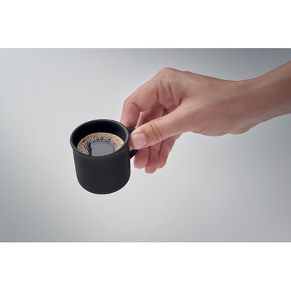 Mano mostrando taza negra de cerámica para café espresso