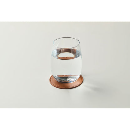 Vaso de agua de cristal sobre posavasos redondo marrón