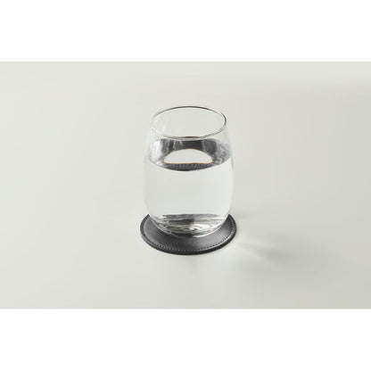 Vaso de agua de cristal sobre posavasos redondo negro