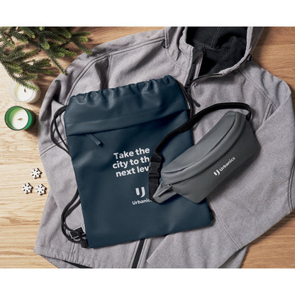 Mochila de cuerdas marino y riñonera con logos sobre chaqueta gris en mesa de madera