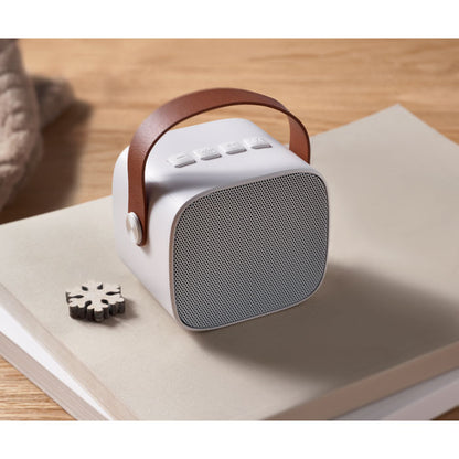Altavoz blanco con asa marrón sobre un libro encima de una mesa de madera