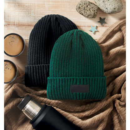 2 gorros de punto, verde y negro con manta y botella sobre mesa de madera