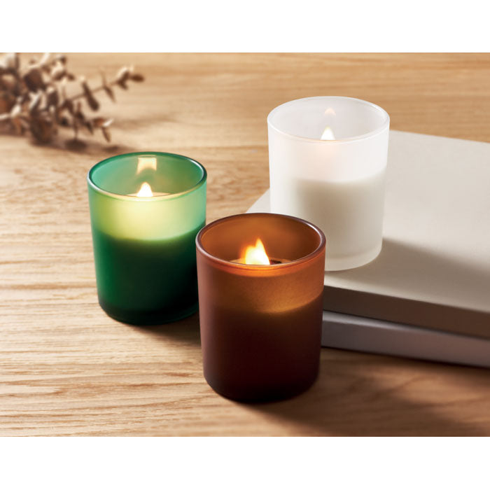 Tres velas encendidas en recipientes de vidrio de diferentes colores, con fondo de madera y libros.