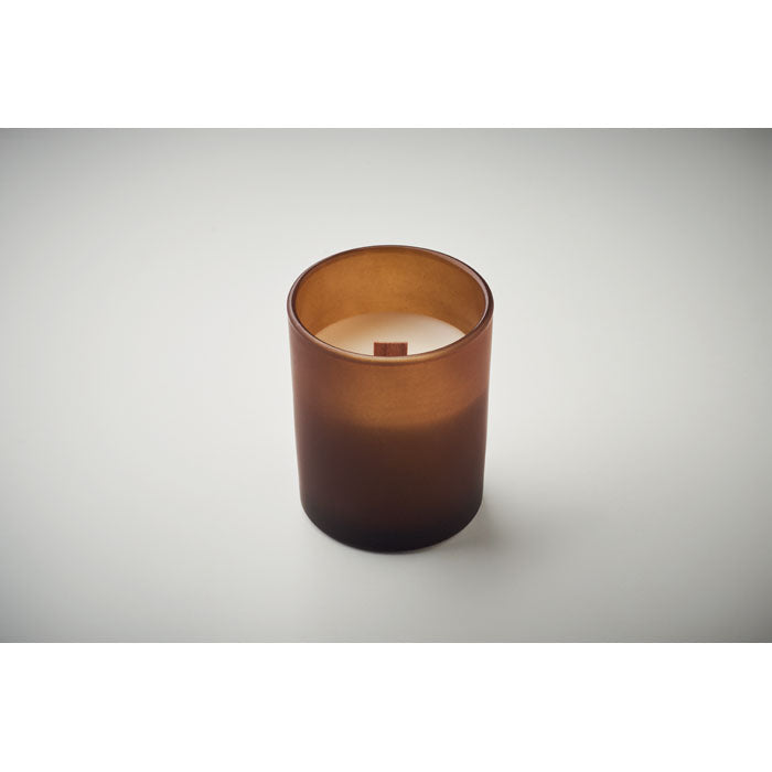 Vista frontal de una vela de cera vegetal en vaso de vidrio marrón, con mecha de madera y fragancia de vainilla.