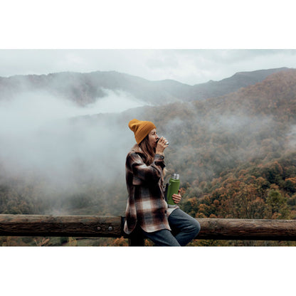 Chica en paisaje otoñal con gorro de lana y botella de acero