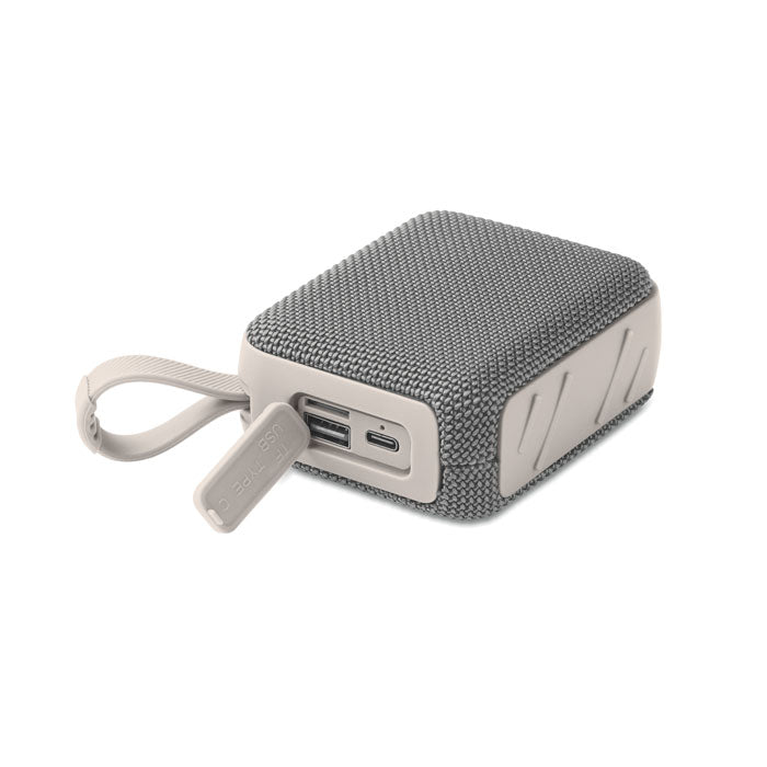 Conexiones visibles en el lateral de un altavoz inalámbrico de 5 W, con puerto USB y detalle del tejido en textura gris.