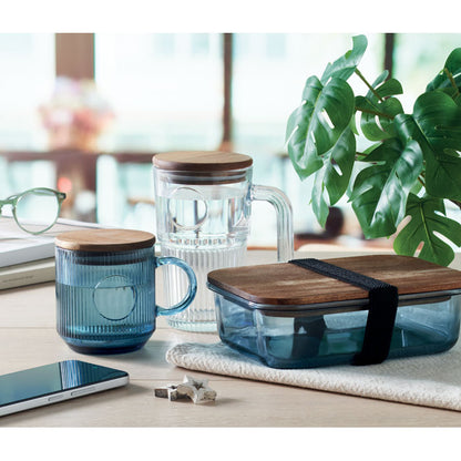 mesa con fiambrera de vidrio azul, taza acanalada de vidrio azul y jarra de cristal