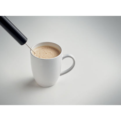 Espumador de leche junto a una taza de café