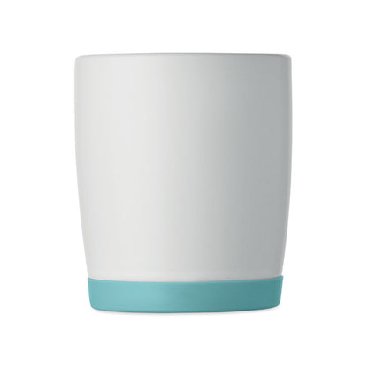Taza blanca mate con base turquesa en mesa con portátil