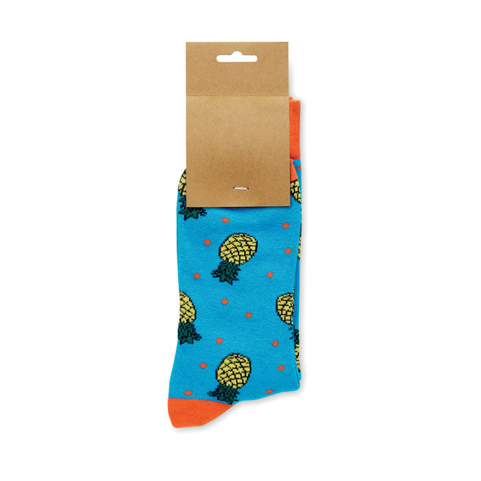 FUNNY M - Calcetines estampados alegres con diseño de piñas en fondo azul y etiqueta de papel kraft.