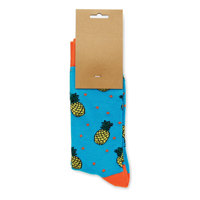FUNNY L - Calcetines estampados alegres con diseño de piñas sobre fondo azul y etiqueta de papel kraft.