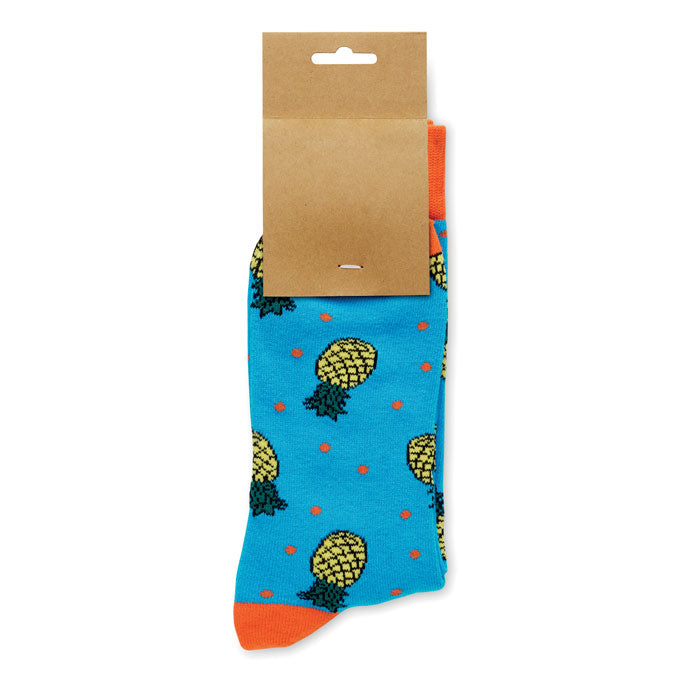 FUNNY L - Calcetines estampados alegres con diseño de piñas sobre fondo azul y etiqueta de papel kraft.