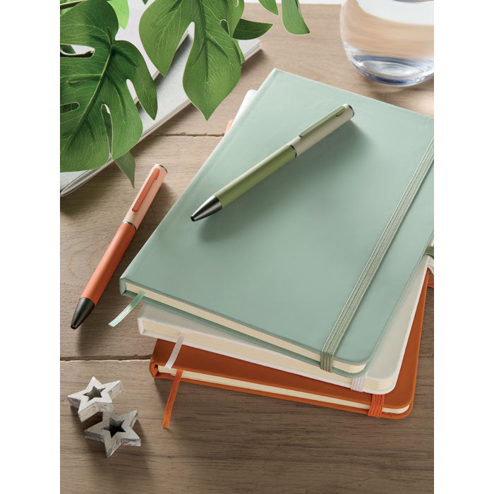 ARCOLOOP - Libreta A5 de PU reciclado apiladas en una mesa con bolígrafos, decoradas con plantas y un vaso.