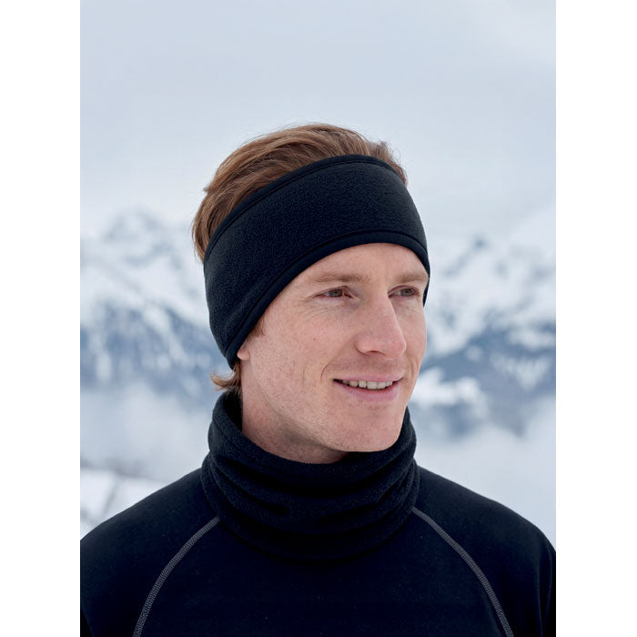 Hombre usando WAVES - Cinta polar para la cabeza negra en un paisaje montañoso nevado, ideal para actividades al aire libre.