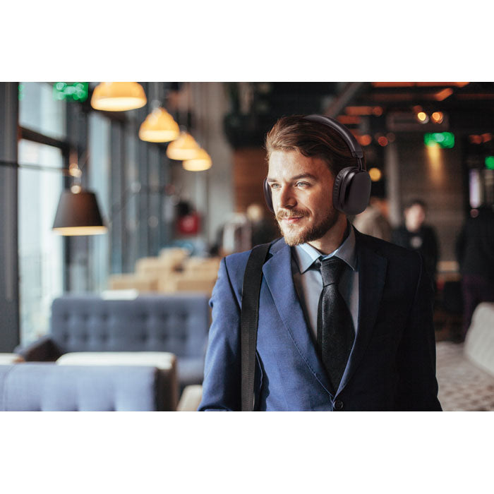 Hombre elegante con auriculares inalámbricos SYNC - en un café moderno, luciendo confiado y profesional.