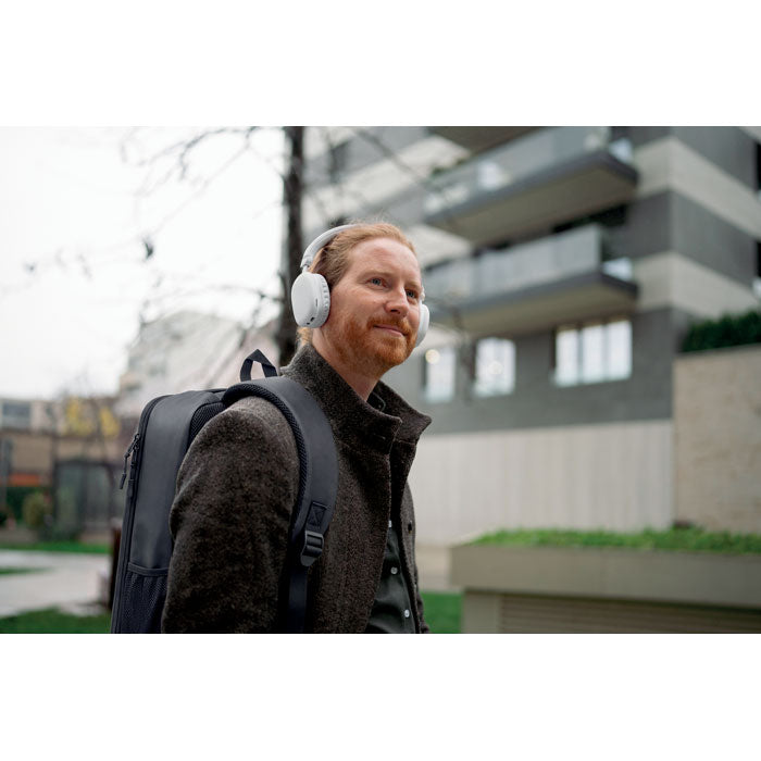 Hombre con mochila NOVIX - Mochila RPET rígida de 15L y auriculares, caminando en un entorno urbano.