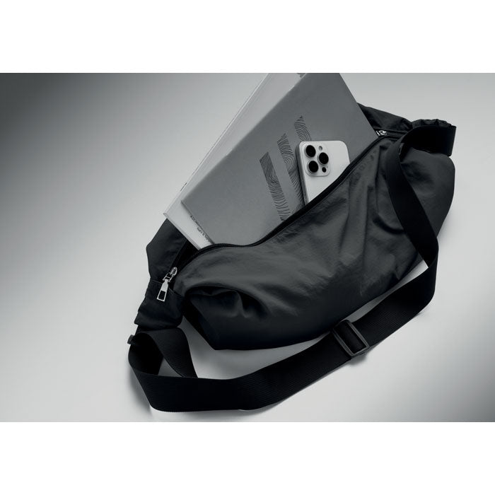 SLING - Bolsa urbana cruzada de nailon sobre fondo gris con cuaderno y teléfono dentro.