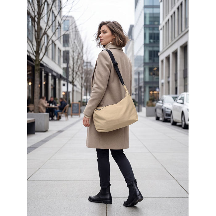 Mujer vestida con abrigo que lleva la SLING - Bolsa urbana cruzada de nailon mientras camina por la ciudad.